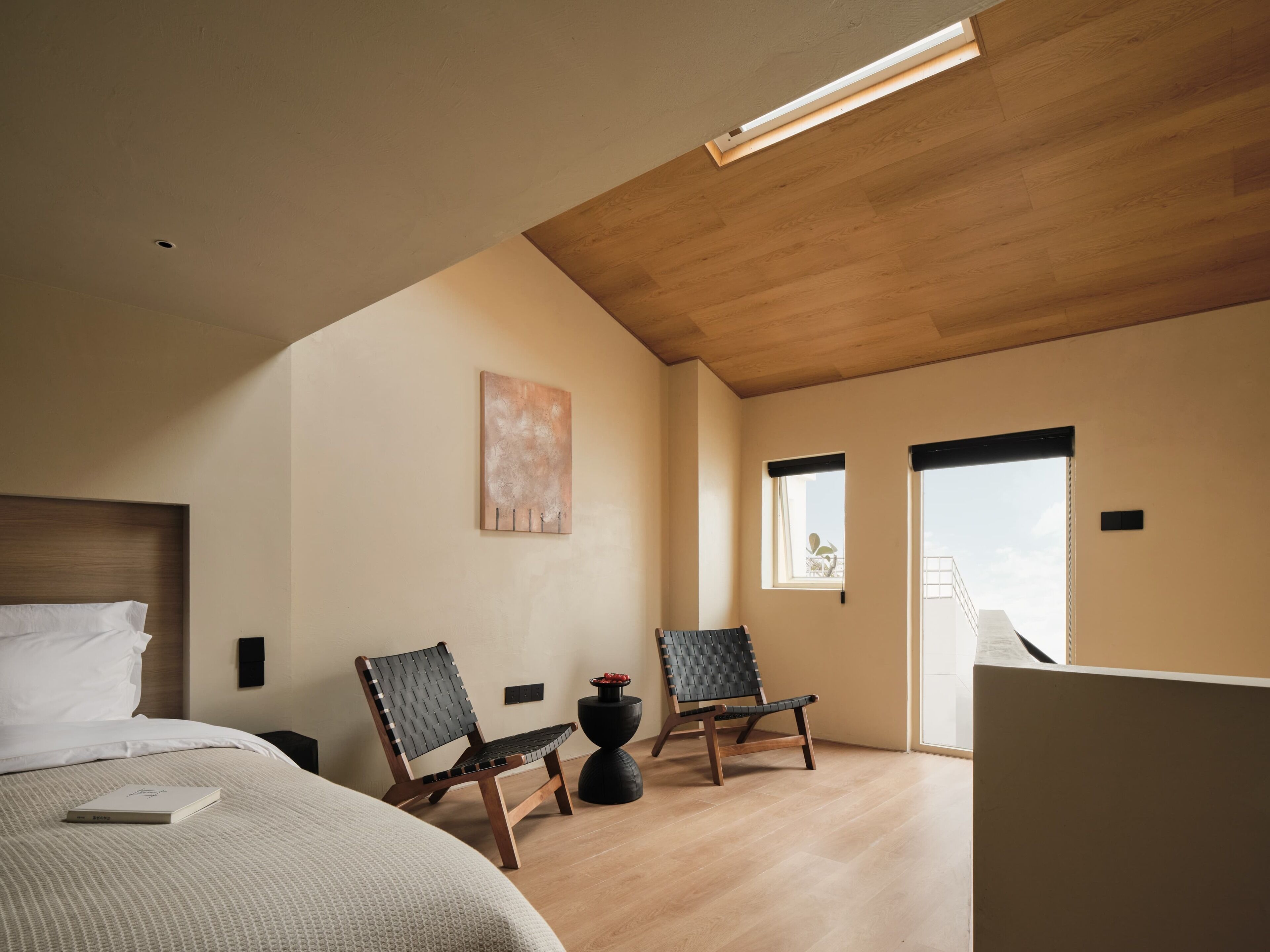 Un dormitorio con una cama, dos sillas, un cuadro y una ventana.