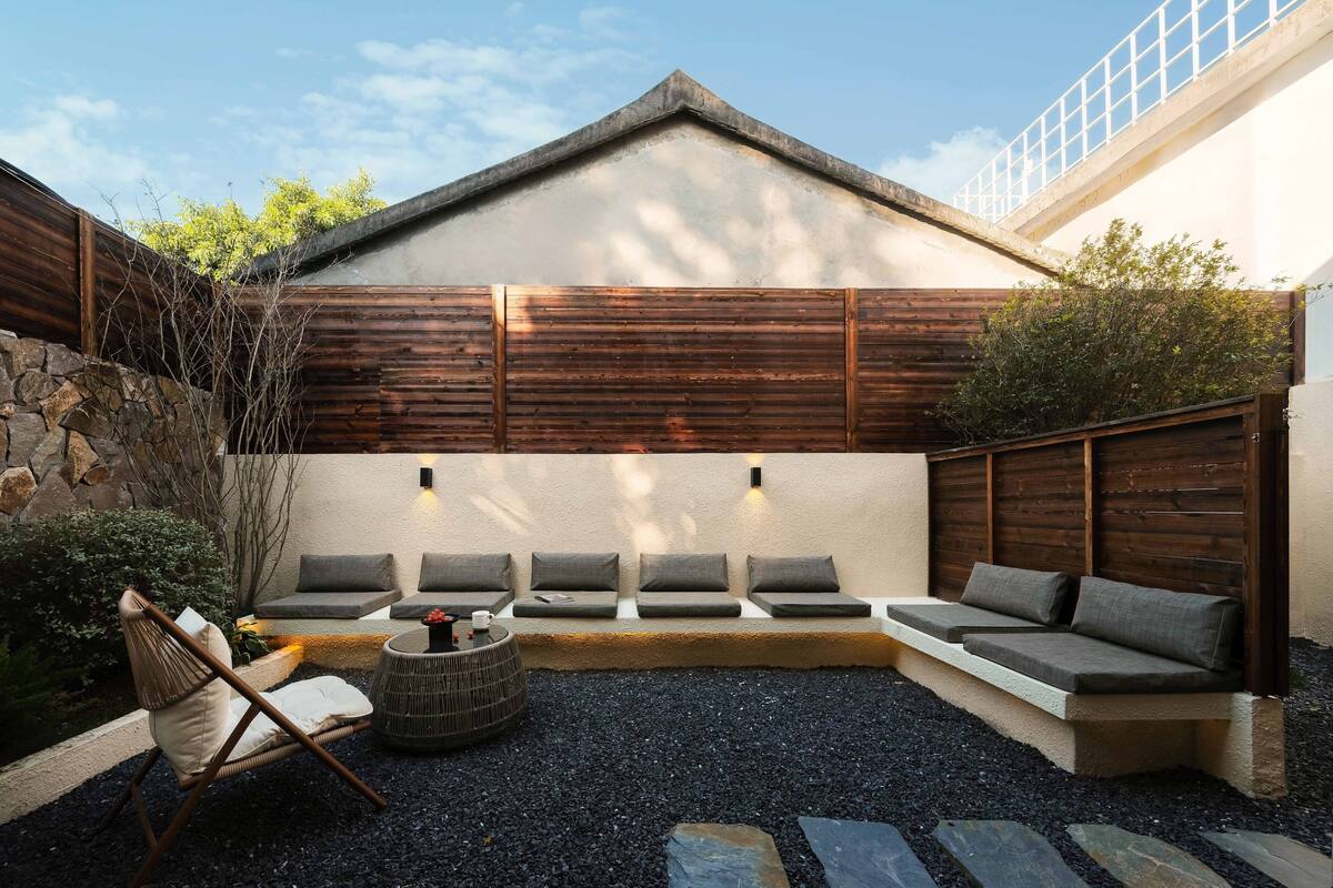 A modern outdoor seating area with a stone wall, wooden fence, and a concrete bench.