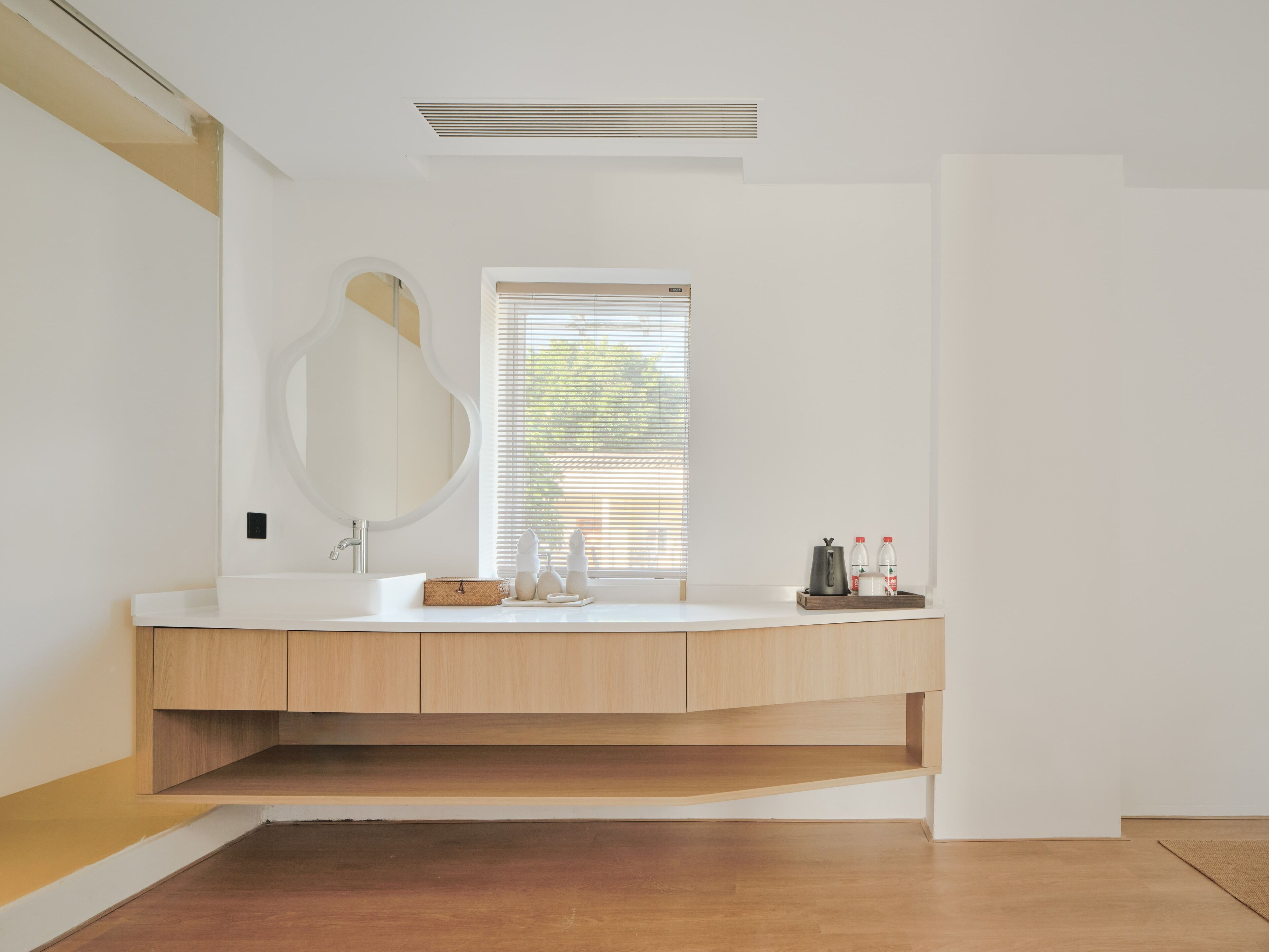 A modern bathroom with a wooden vanity, a large mirror, and a window with blinds.