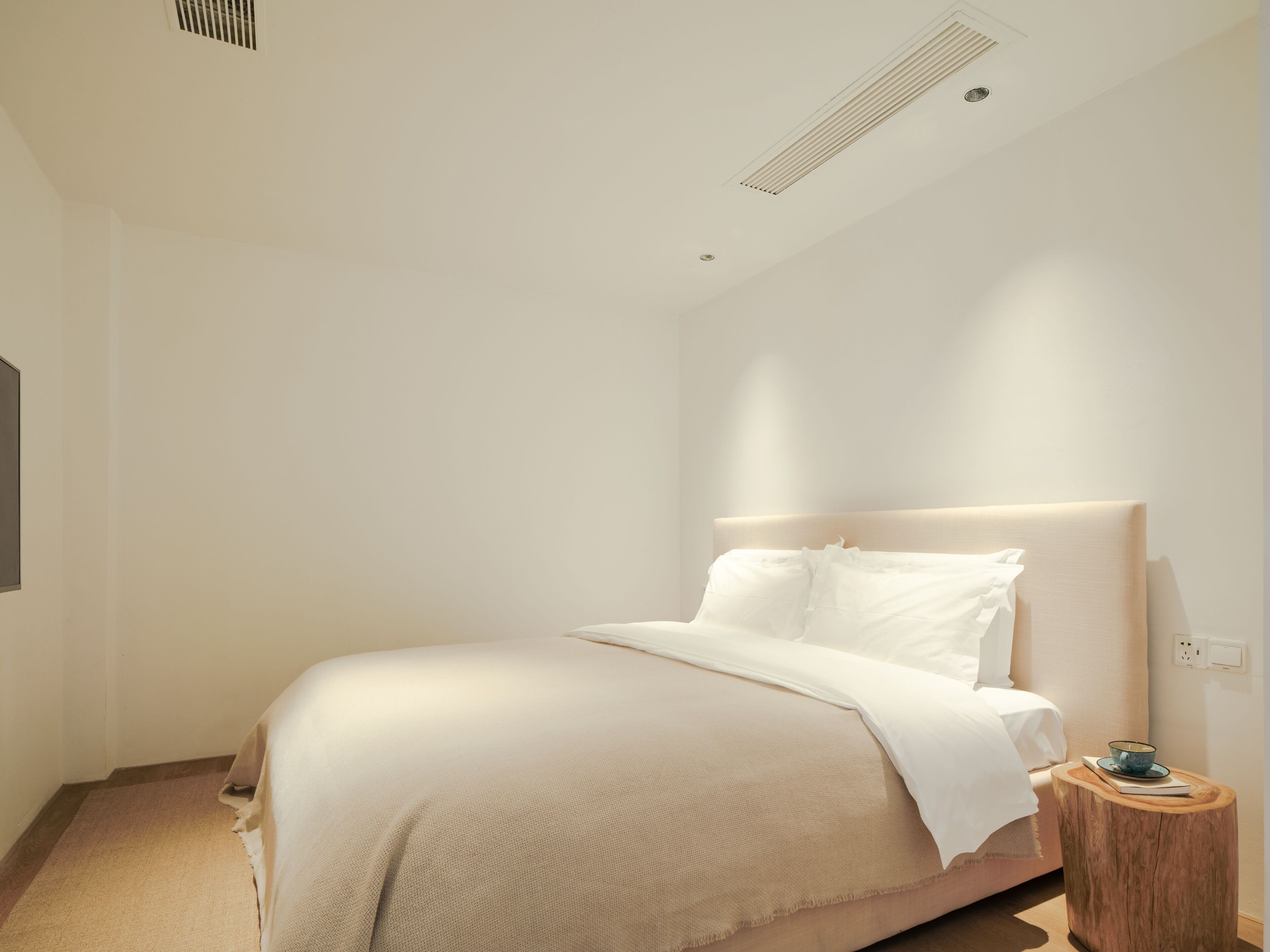 Een minimalistisch ingerichte slaapkamer met een bed, nachtkastje en een stopcontact.
