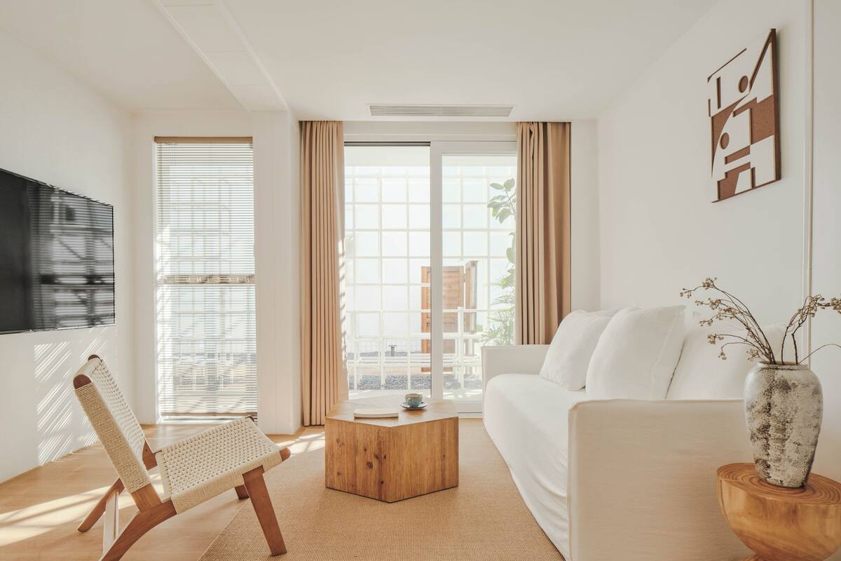 A modern living room with a white sofa, a wooden coffee table, and a woven chair.