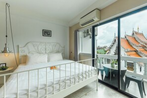A bedroom with a white metal bed, a nightstand, a bedside lamp, and a view of traditional architecture through a glass door. - Fav Inn Town  (Chiang Mai)