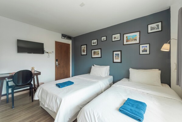 A hotel room with two beds, a desk, a chair, a flat-screen TV, and several framed pictures on the wall. - Fav Inn Town  (Chiang Mai)