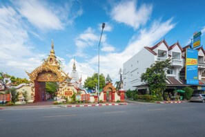 En gatubild med en traditionell thailändsk tempelport, en modern byggnad och en bil som står parkerad vid sidan av vägen.