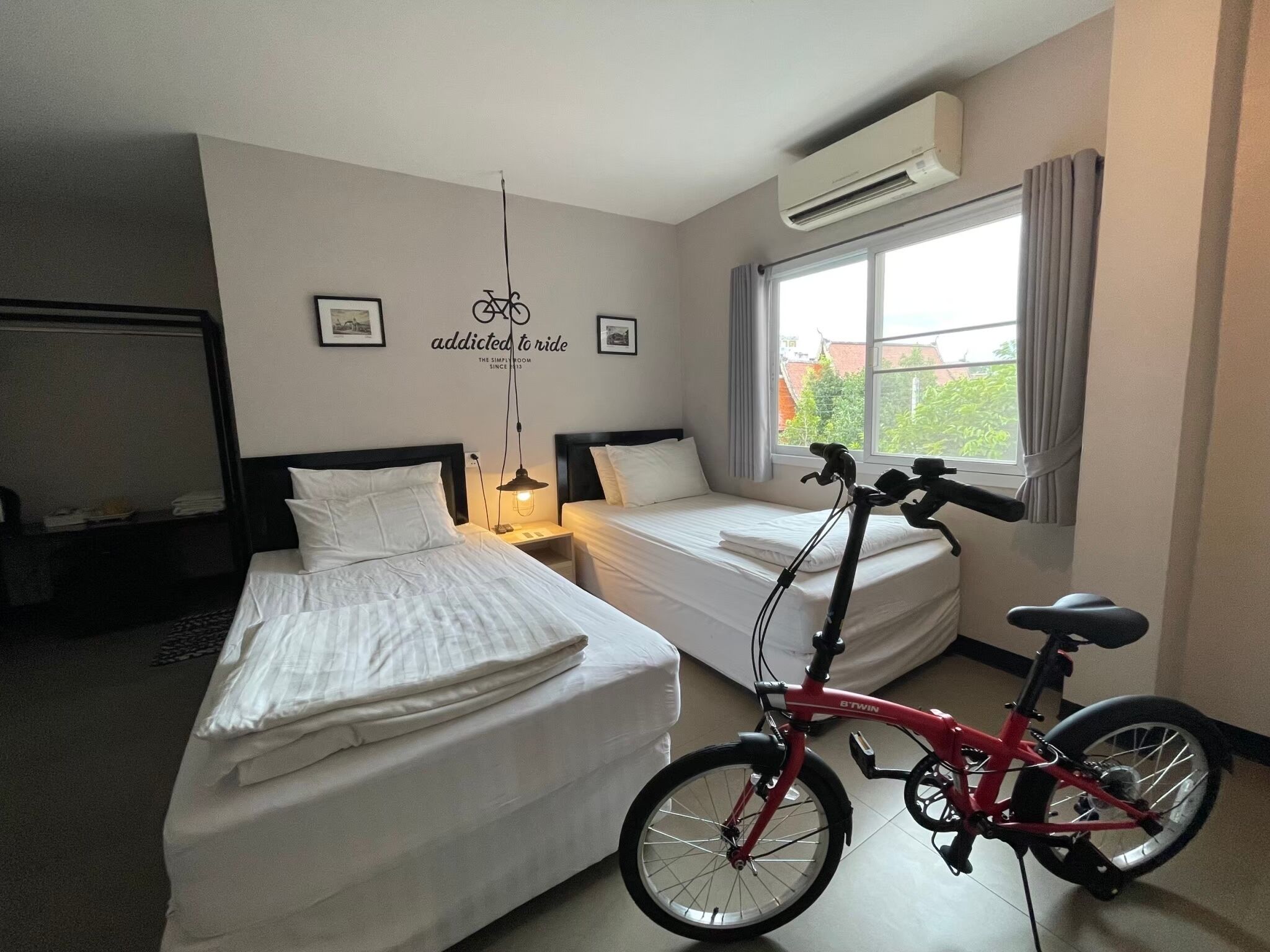 A hotel room with two beds, a bicycle, and a window with curtains.