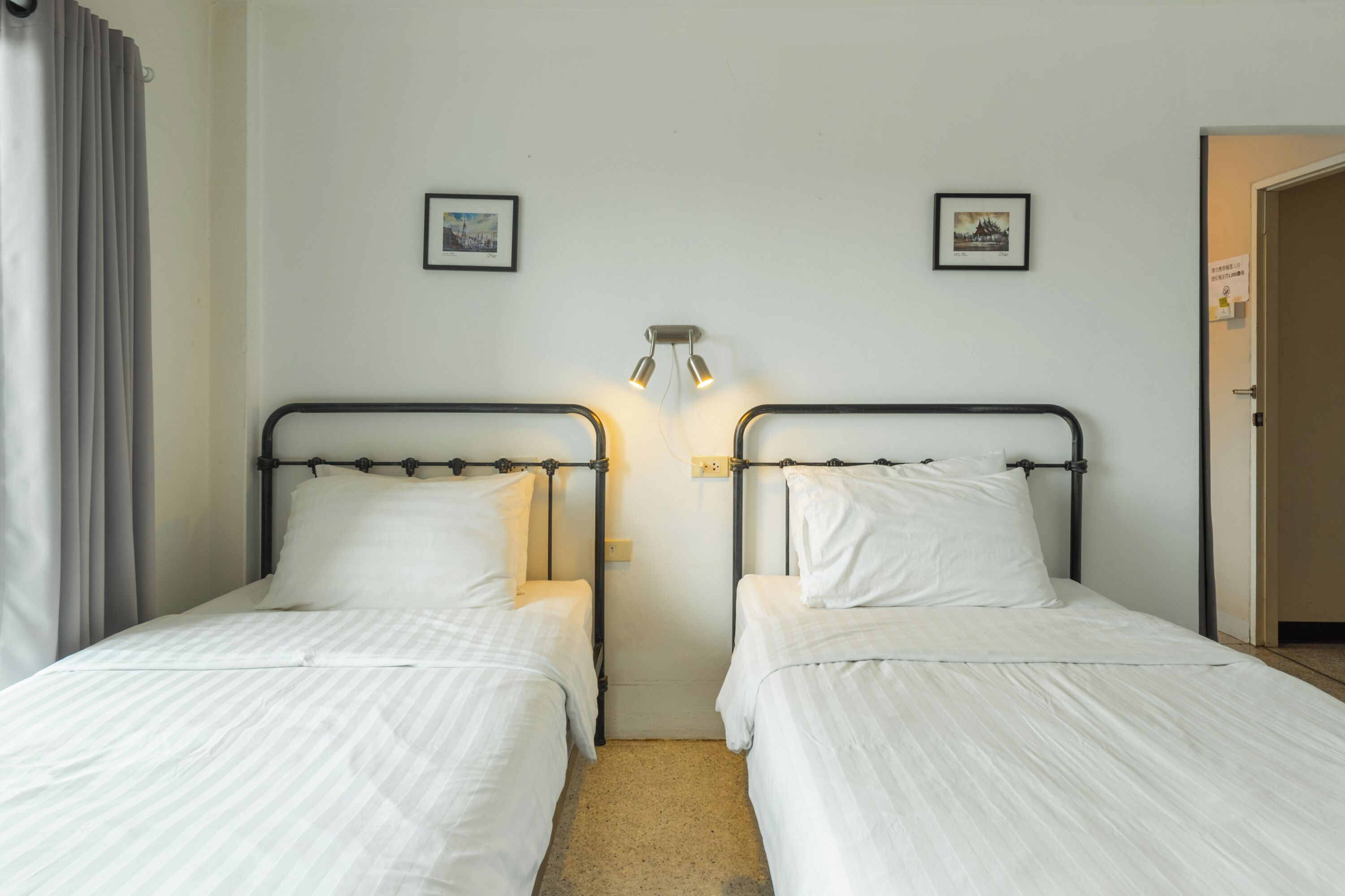 A room with two single beds, a wall-mounted light fixture, and two framed pictures.