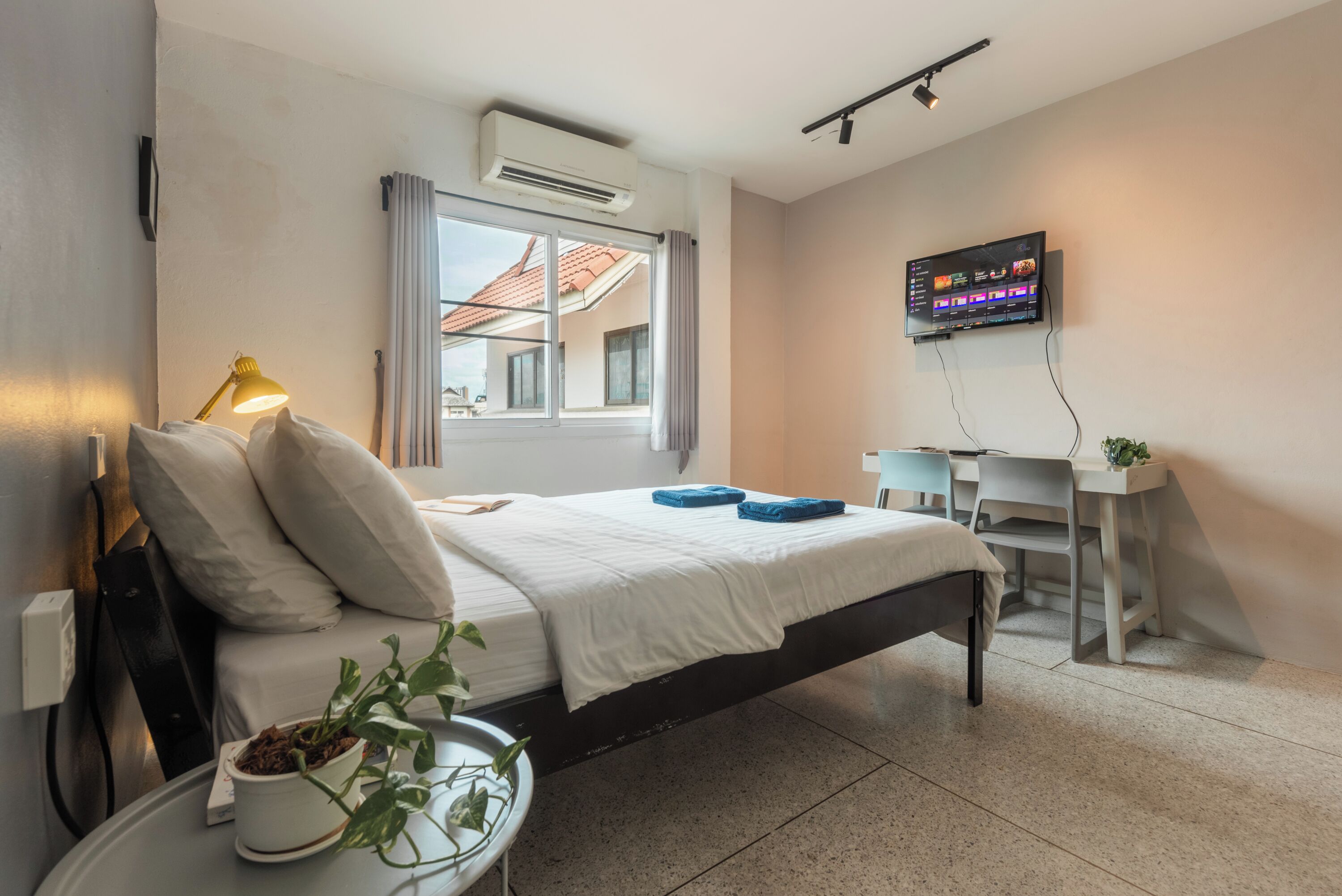 Una habitación de hotel moderna con cama, lámpara de noche, aire acondicionado, televisión y un pequeño escritorio.