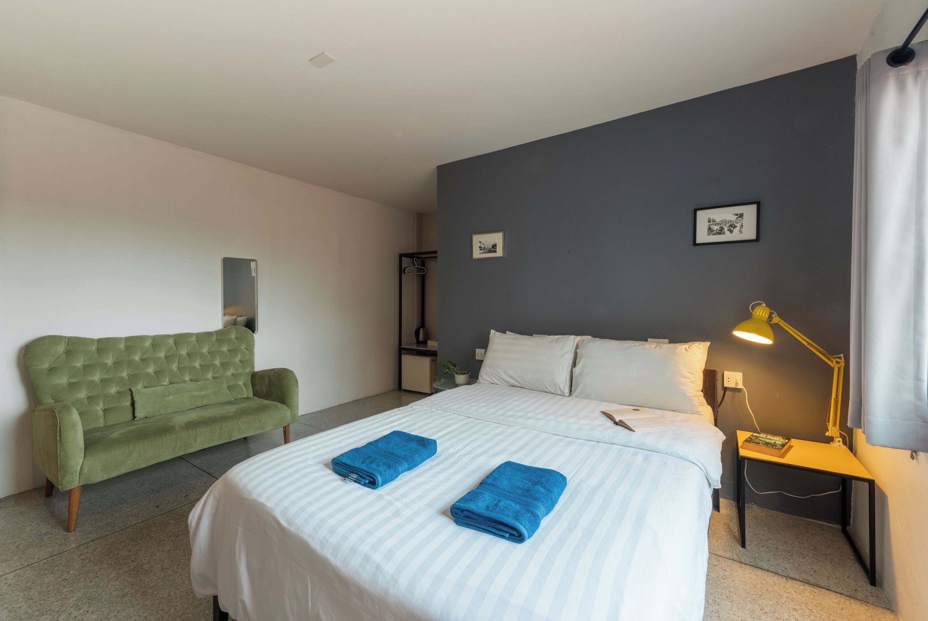 Hotelkamer met een bed, een groene bank, twee blauwe handdoeken, een nachtkastje met een lamp en twee ingelijste foto's aan de muur.