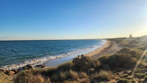 Ein Küstenstrand mit Kies, grasbewachsenen Dünen und blauem Himmel.