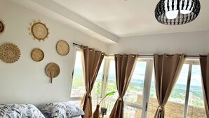 Ein Schlafzimmer mit einem Bett, mehreren Wanddekorationen, einer Deckenleuchte und großen Fenstern mit Vorhängen.