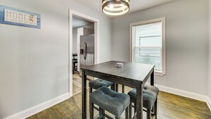 Un coin repas avec une table en bois foncé et quatre tabourets de bar rembourrés. Un luminaire suspendu moderne est accroché au-dessus de la table.