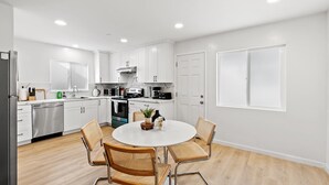 A modern kitchen with white cabinets, stainless steel appliances, and a round dining table with four chairs. - 222 - New, Stylish Quiet 2B1B w/ Yard near Stanford (Redwood City)