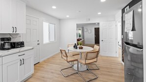 A modern kitchen with white cabinets, a dining table with four chairs, and a refrigerator. - 222 - New, Stylish Quiet 2B1B w/ Yard near Stanford (Redwood City)