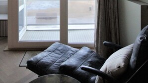 Een kamer met een schuifglazen deur die leidt naar een balkon, een leren bank en een kleine tafel.