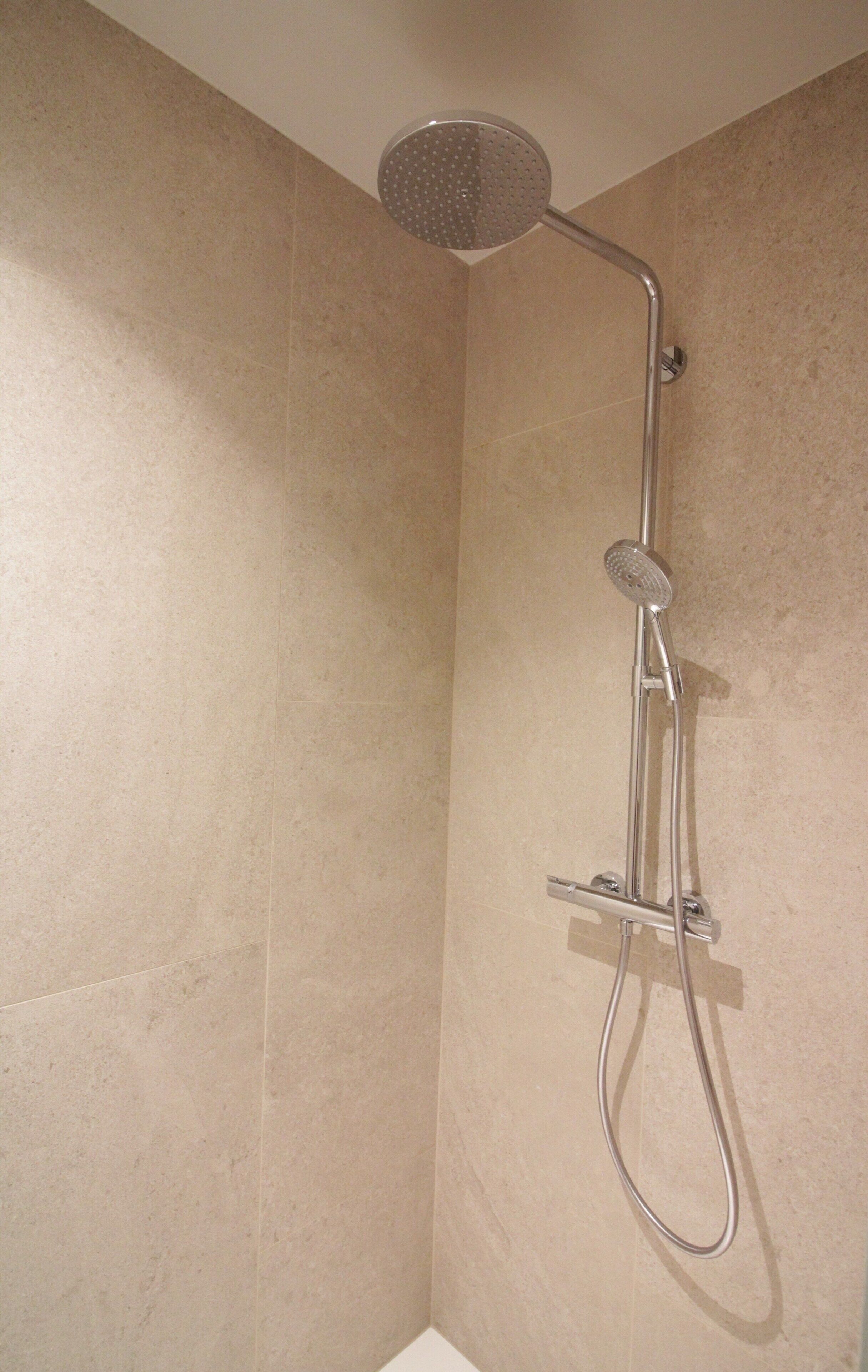 Une douche d’angle équipée d’un pommeau de douche à main et d’un panneau de commande fixé au mur.