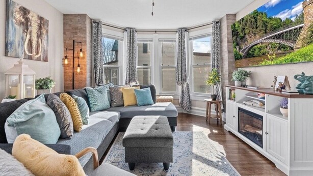 A modern living room with a sectional sofa, a fireplace, and a large window with curtains. - Charming Wisconsin Dells, Devil’s Lake, & Circus World Retreat! (Baraboo)
