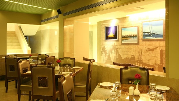 A restaurant with tables set for dining, chairs, and a staircase in the background. - The Maharaja Business Hotel (Mumbai)