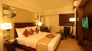 A hotel room with a large bed, bedside tables, a desk, a chair, a TV, and artwork on the walls. - The Maharaja Business Hotel (Mumbai)