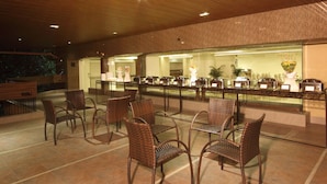 A buffet area with wicker chairs and tables, a glass display case with food items, and a brick wall in the background. - The Maharaja Business Hotel (Mumbai)