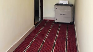 A narrow hallway with a red carpet, a door at the end, and a small cabinet with a box on top. - Sai Home Stay (Coimbatore)