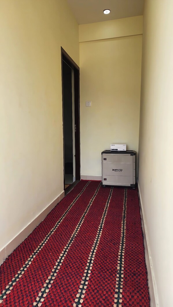 A narrow hallway with a red carpet, a door at the end, and a small cabinet with a box on top. - Sai Home Stay (Coimbatore)