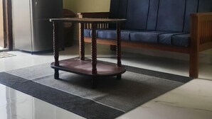 A living room with a sofa, a small wooden table, a refrigerator, and a tiled floor. - Sai Home Stay (Coimbatore)
