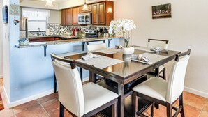 Una cocina moderna con armarios de madera, microondas y comedor con mesa de vidrio y cuatro sillas.