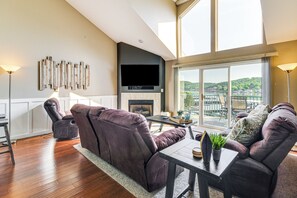 Een moderne woonkamer met een open haard, een grote televisie en uitzicht op een balkon met buitenmeubilair.