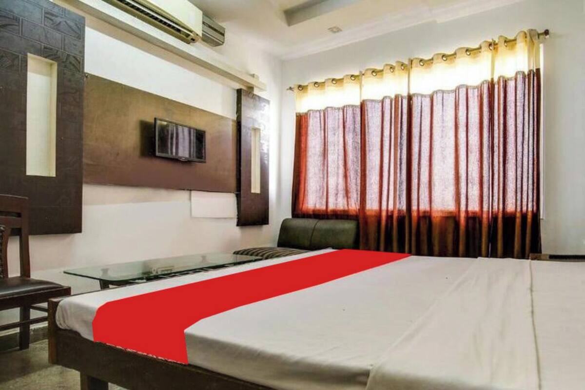 A hotel room with a bed, a desk, a chair, a television, and a window with curtains.