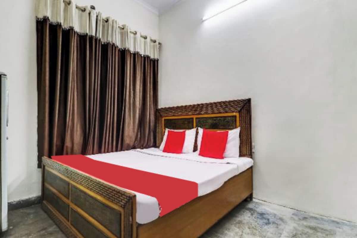 A single bed with a wooden frame and a red and white bedspread, positioned against a wall with a marble floor.
