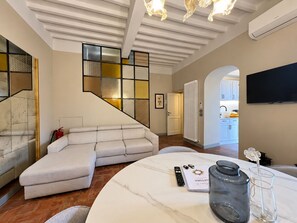 A modern living room with a sectional sofa, a round marble table, and a flat-screen TV mounted on the wall.