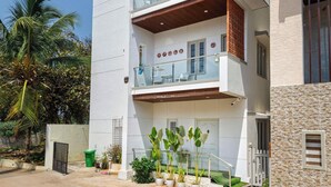 A modern two-story residential building with a balcony, a garage, and a small garden area with potted plants. - Golden Ivory by Red Olive (Bengaluru)