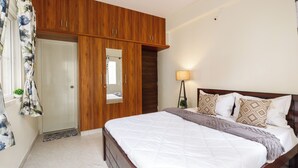 A bedroom with a large bed, wooden wardrobe, and a mirror. - The City Nova Apartment Koramangla (Bengaluru)