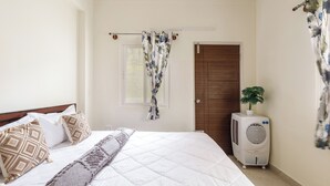 A bedroom with a bed, pillows, a blanket, a window, a door, a radiator, and a plant. - The City Nova Apartment Koramangla (Bengaluru)