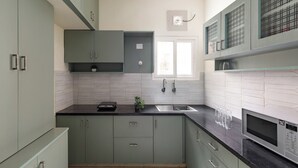 A modern kitchen with green cabinets, a black countertop, a microwave, and a window above the sink. - The City Nova Apartment Koramangla (Bengaluru)