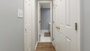 A narrow hallway with white doors on both sides, leading to a bathroom with a white toilet and a towel rack. - Cozy + Connected • Central, office space with fast wifi, family and pet friendly (Greensboro)