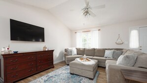A living room with a sectional sofa, a wooden dresser, a flat-screen TV, and a ceiling fan. - Cozy + Connected • Central, office space with fast wifi, family and pet friendly (Greensboro)