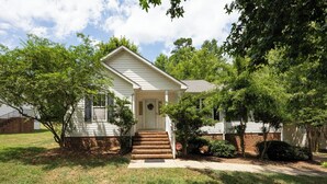 A two-story house with a front porch, a small front yard, and a brick foundation. - Cozy + Connected • Central, office space with fast wifi, family and pet friendly (Greensboro)