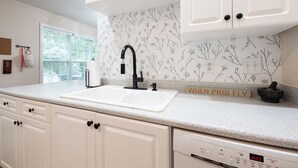 A kitchen with white cabinetry, a black faucet, a white countertop, and a backsplash with a nature pattern. - Cozy + Connected • Central, office space with fast wifi, family and pet friendly (Greensboro)