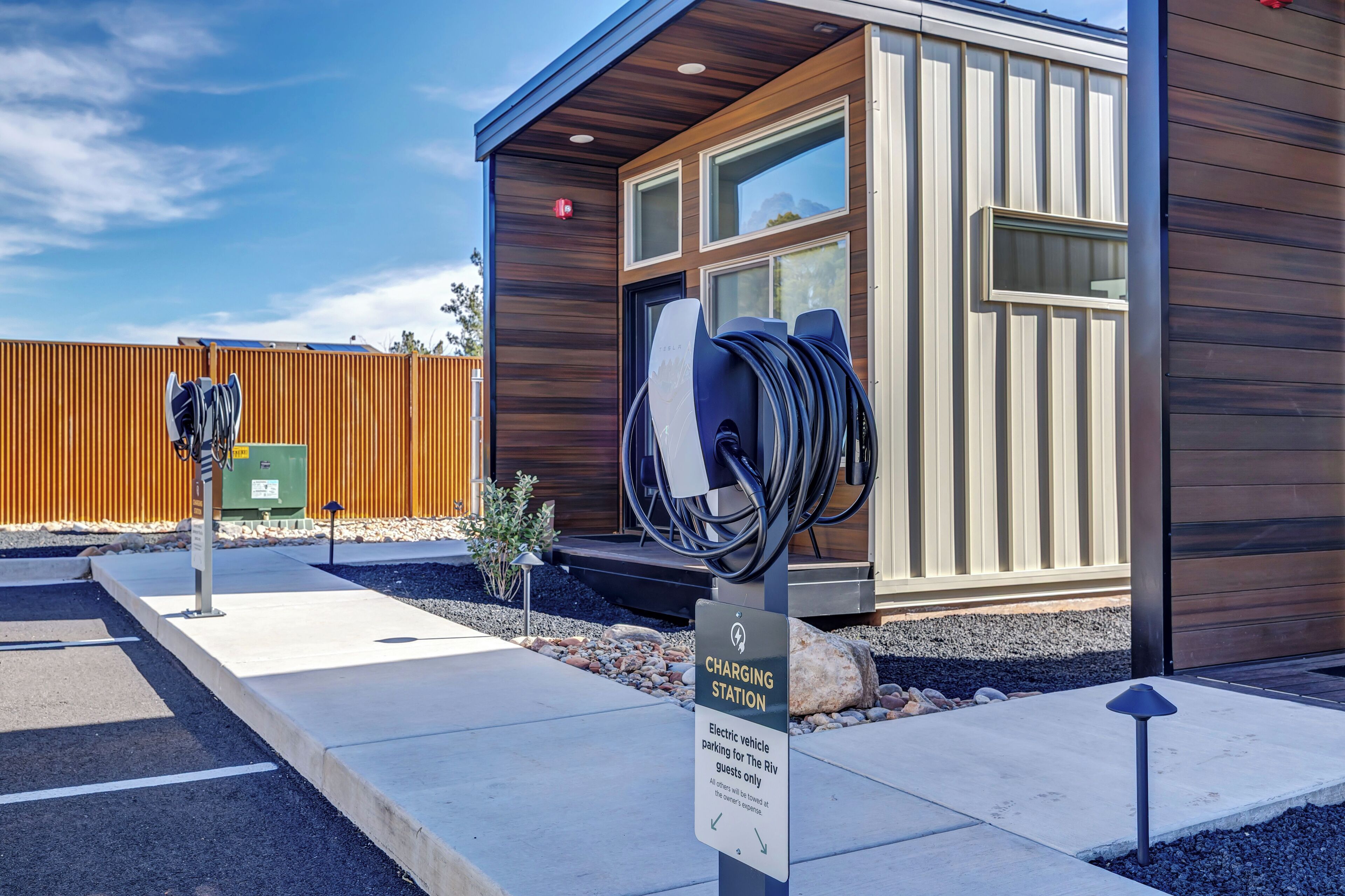 A modern building with a charging station for electric vehicles, a sign indicating it's for guests only, and a wooden fence in the background.