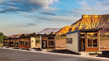 A row of modern, single-story cabins with large windows, set against a mountainous backdrop.