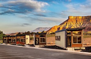 A row of modern, single-story cabins with large windows, set against a mountainous backdrop.