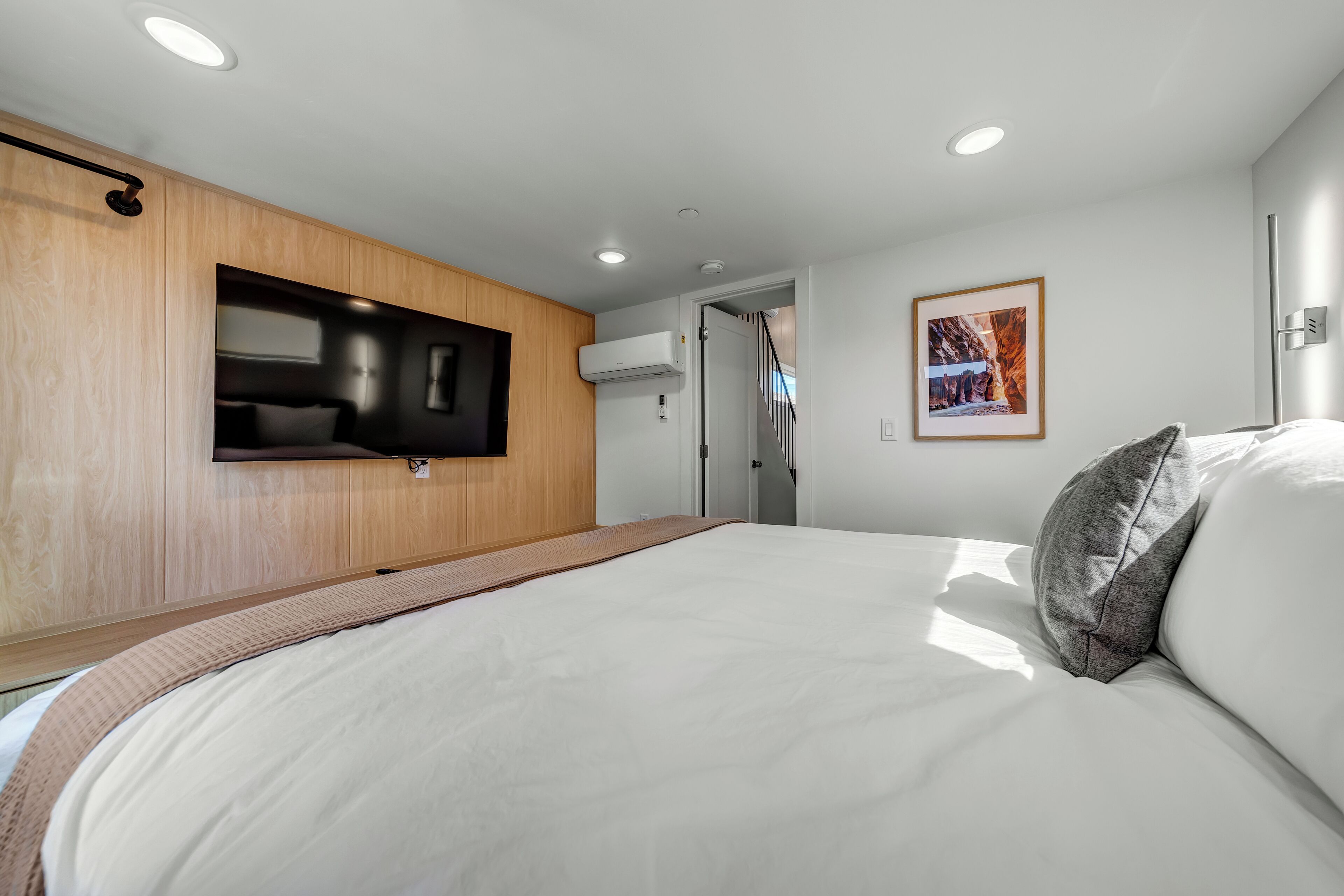Un dormitorio moderno con una cama, un televisor montado y un cuadro en la pared.