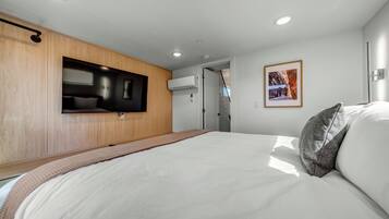 Un dormitorio moderno con una cama, un televisor montado y un cuadro en la pared.