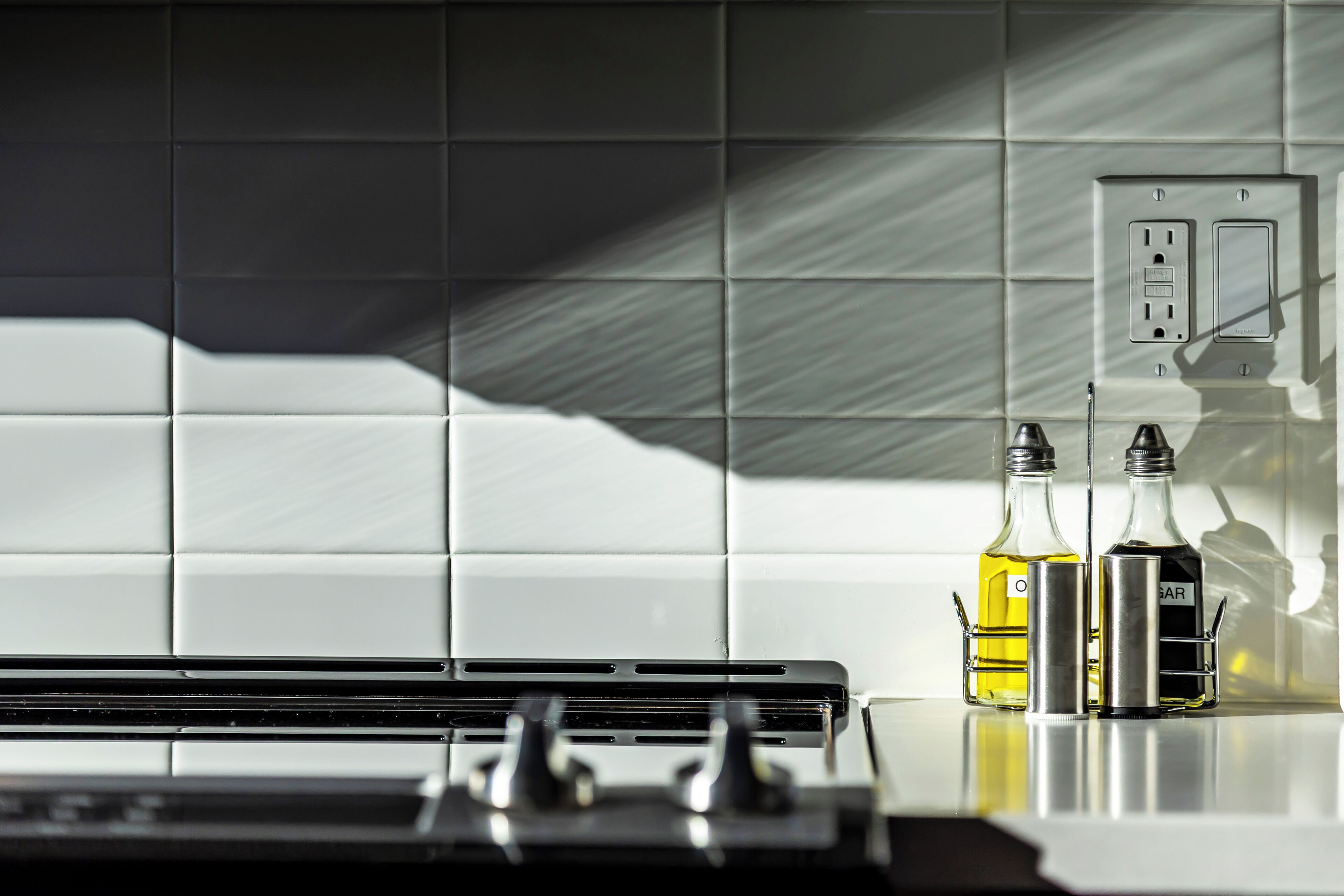 A kitchen with white tiled backsplash, a stove, and two bottles on the counter.