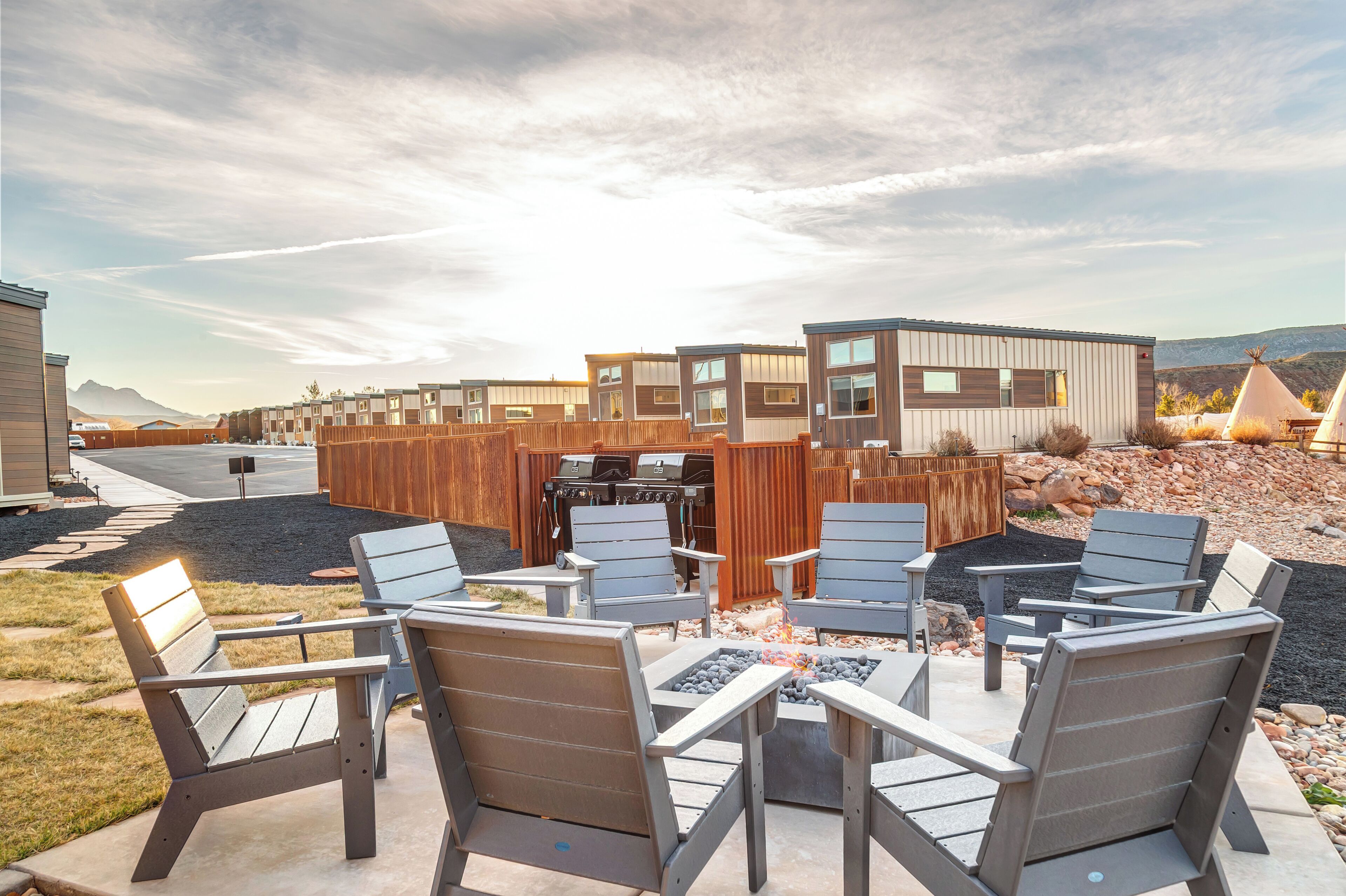 Eine moderne Terrassenanlage im Freien mit Adirondack-Stühlen, einem Grill und einer Feuerstelle.