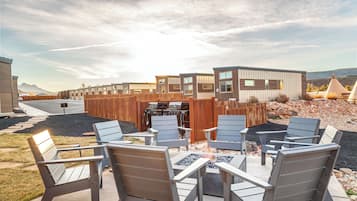 A modern outdoor patio with Adirondack chairs, a grill, and a fire pit.