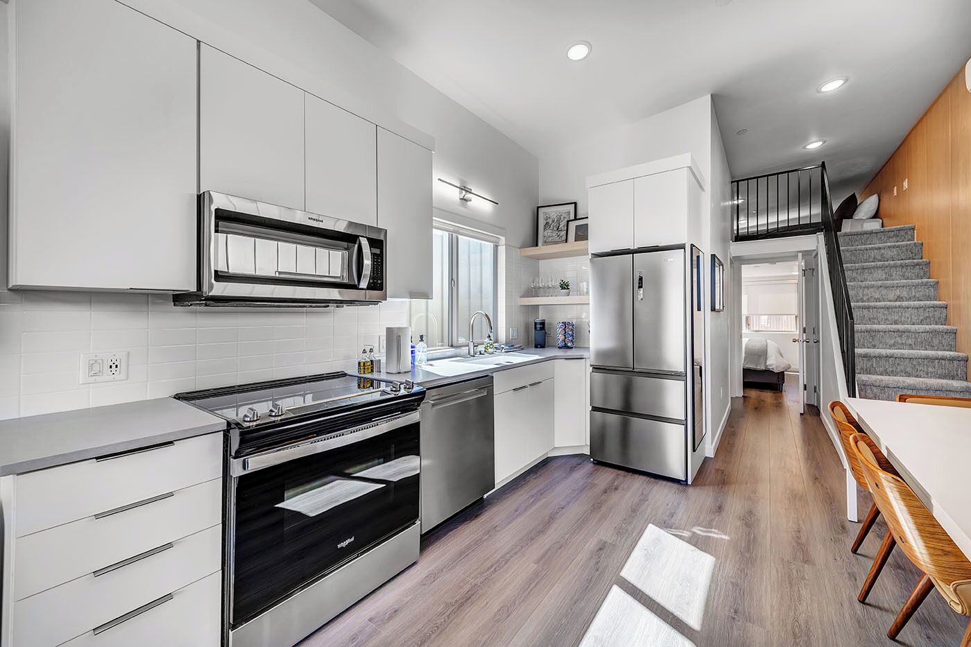 A modern kitchen with stainless steel appliances, a dining area with a wooden table, and a staircase leading to a loft bedroom.