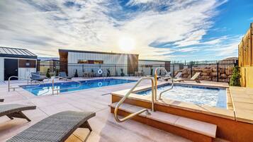 Un espace piscine aménagé sur le toit, avec des chaises longues, un jacuzzi et un bâtiment portant une enseigne.