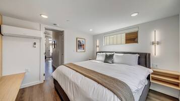 Une chambre à coucher moderne, dotée d’un grand lit, de tables de chevet, d’une lampe fixée au mur et d’un ventilateur de plafond.